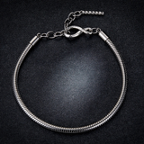 Charm Armband mit Karabinerverschluss in der Form eines Unendlichkeitssymbols. Das Charm-Armband ist auf einem dunklen, glitzernden hintergrund zu sehen. 